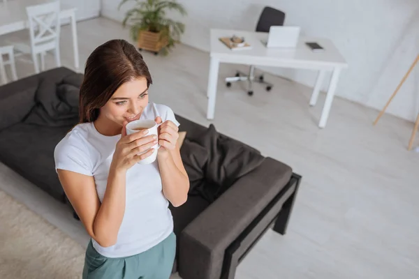 Blick auf attraktive Frau, die Tee im Wohnzimmer trinkt — Stockfoto