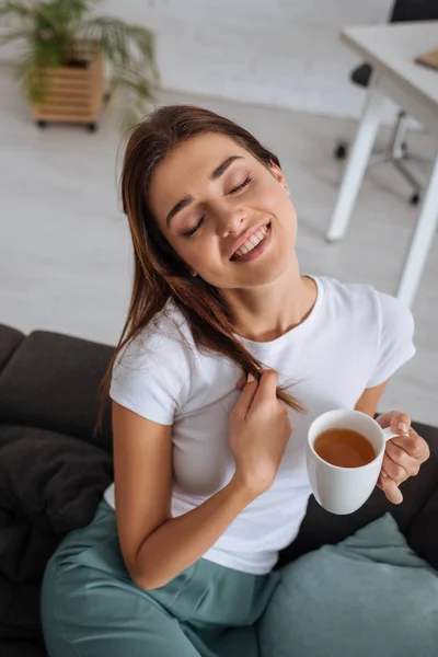 Jovem mulher segurando xícara com chá enquanto refrigerando no sofá na sala de estar — Fotografia de Stock