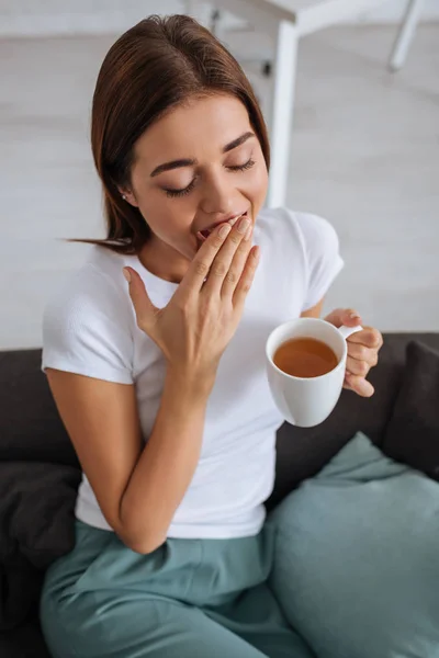 Overhead view of tired woman yawning and cover mouth while holding cup of tea — Stock Photo