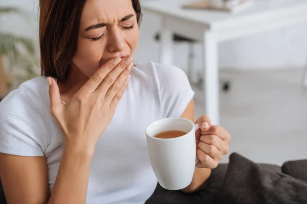 Tired woman yawning and cover mouth while holding cup — Stock Photo