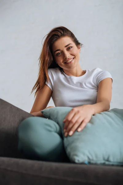 Селективное внимание веселой девушки, смотрящей в камеру, замерзающей на диване — стоковое фото