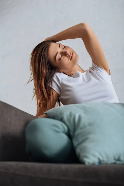 Selective focus of dreamy girl with closed eyes relaxing on sofa — Stock Photo