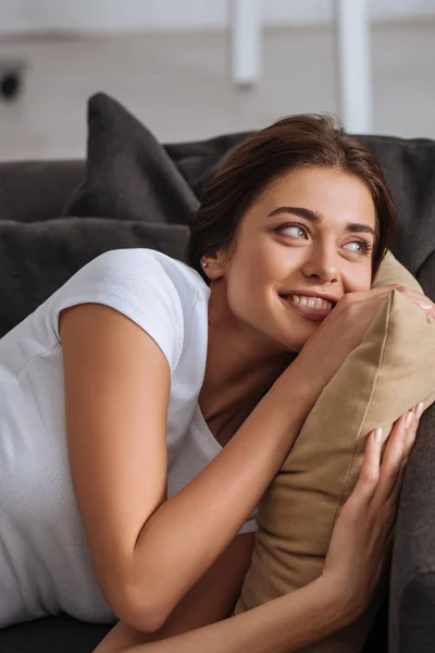 Menina sonhadora sorrindo enquanto deitado no sofá e almofada comovente — Fotografia de Stock