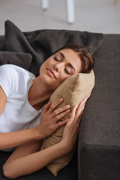 Chica de ensueño con los ojos cerrados acostado en el sofá y tocando almohada - foto de stock