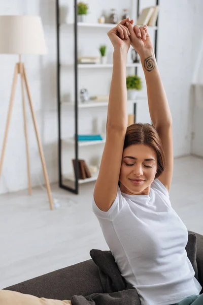 Young tattooed woman with outstretched hands relaxing in living room — Stock Photo