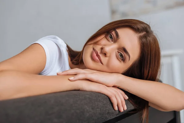 Happy young woman looking at camera while relaxing on sofa in living room — Stock Photo