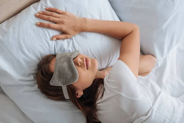 Vista dall'alto di giovane donna in maschera per gli occhi a riposo in camera da letto — Foto stock