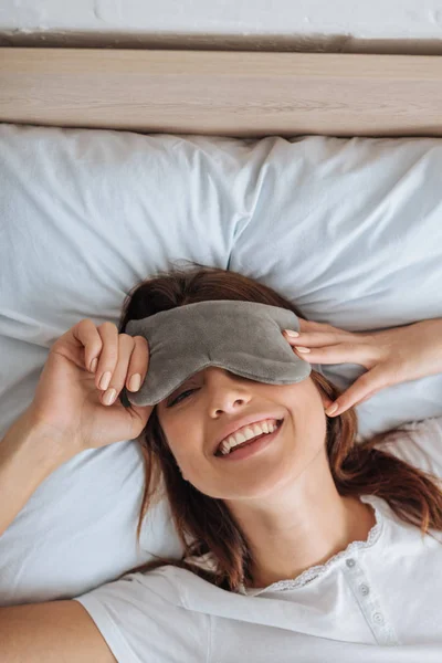 Вид зверху щасливої молодої жінки в масці для очей, що відпочиває в спальні — стокове фото