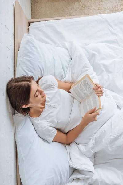 Blick von oben auf glückliche Mädchen, die Buch lesen, während sie im Bett chillen — Stockfoto