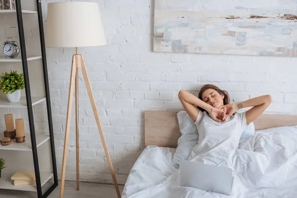 Verträumte Frau chillt im Bett neben Laptop — Stockfoto