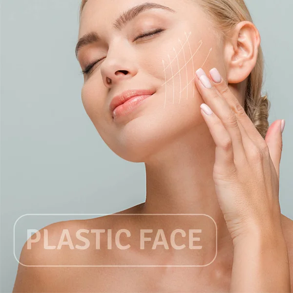 Mujer sonriente tocando la cara con marcas de lifting facial aisladas en gris con ilustración de la cara de plástico - foto de stock