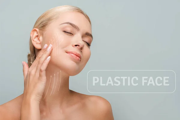 Mujer sonriente tocando la cara con marcas de lifting facial aisladas en gris con ilustración de la cara de plástico - foto de stock