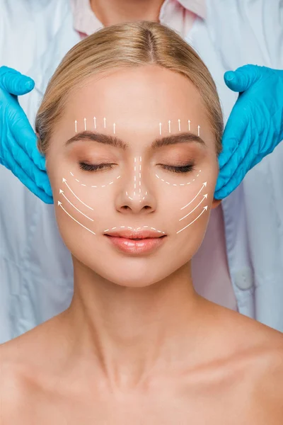 Vue recadrée de l'esthéticienne en gants de latex bleu touchant les tempes de la femme avec les yeux fermés et des marques de chirurgie plastique sur le visage — Photo de stock