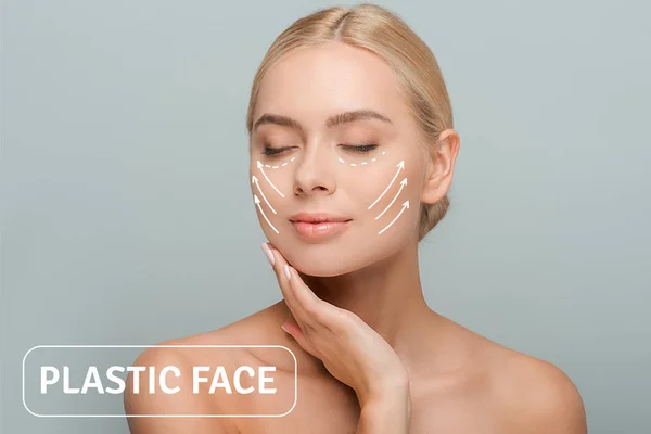 Jovem mulher bonita com olhos fechados tocando rosto com marcas de cirurgia plástica isolado em cinza — Fotografia de Stock
