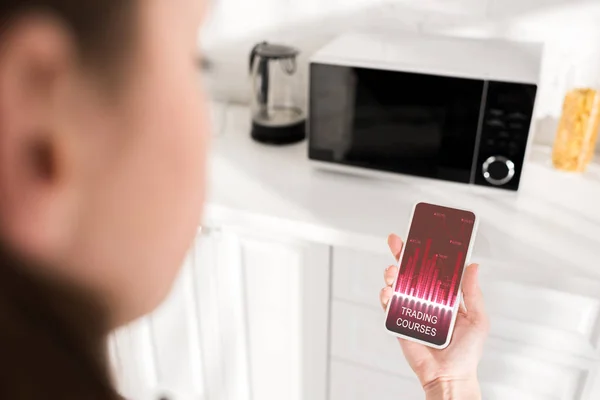 Selective focus of woman holding smartphone with trading courses app and microwave on background — Stock Photo