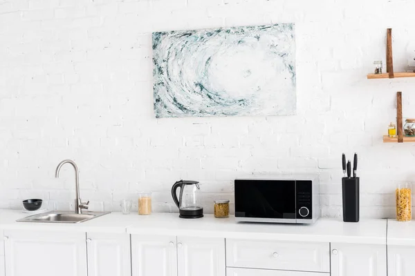 Microwave, electric kettle, pasta, knives and sink on surface in kitchen — Stock Photo