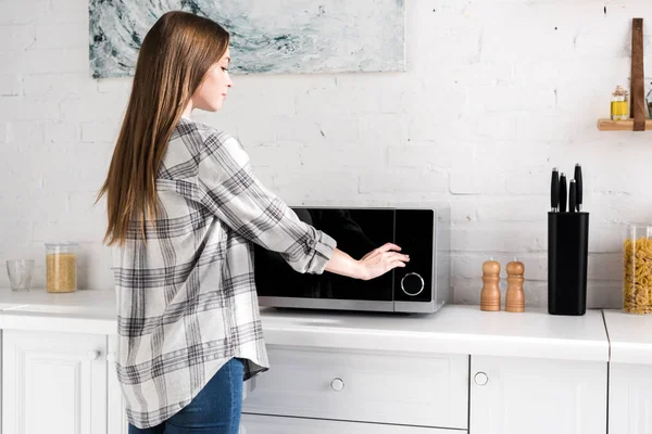 Vista laterale di donna attraente utilizzando forno a microonde in cucina — Foto stock