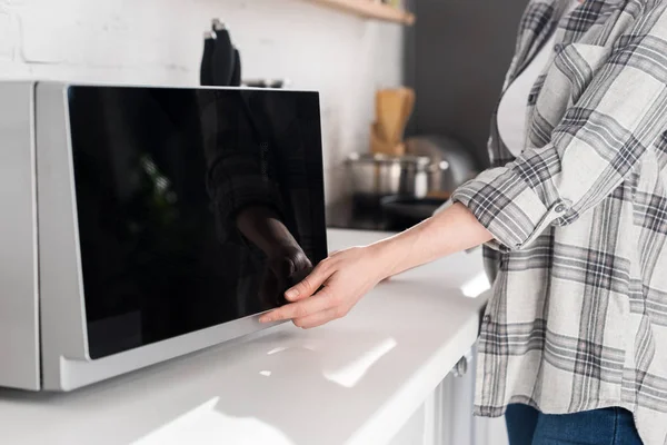 Cropped view of woman in shirt using microwave in kitchen — Stock Photo