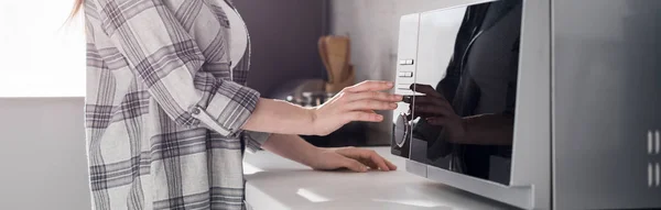 Panoramic shot of woman in shirt using microwave in kitchen — Stock Photo