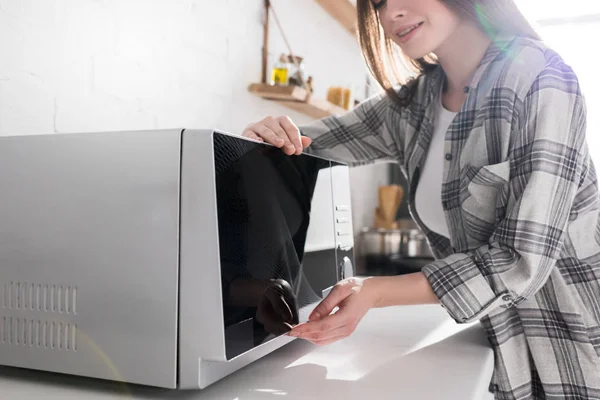 Vista ritagliata di donna sorridente utilizzando il forno a microonde in cucina — Foto stock