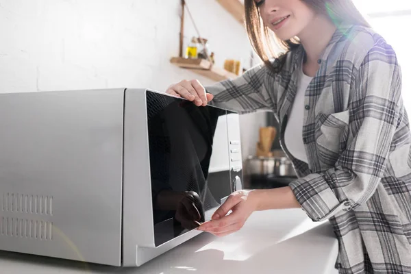 Vista recortada de la mujer sonriente usando microondas en la cocina - foto de stock