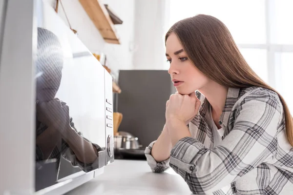 Femme chère en chemise regardant micro-ondes dans la cuisine — Photo de stock