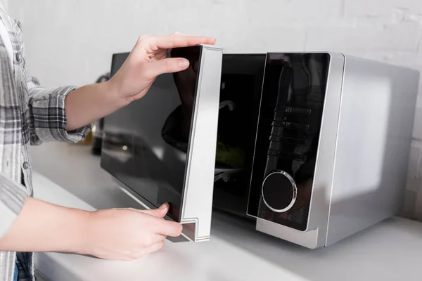Обрезанный вид женщины закрывая дверь микроволновой печи на кухне — стоковое фото