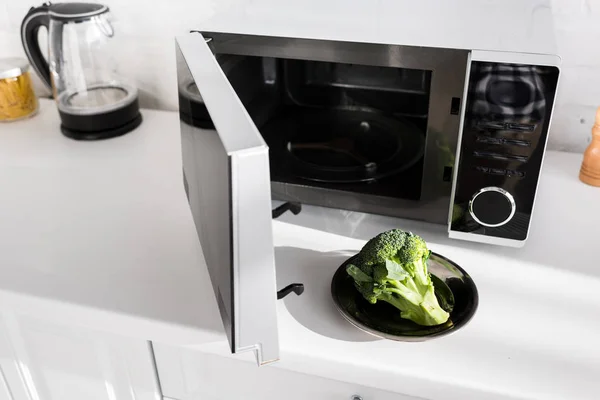 Teller mit Brokkoli auf Teller in der Nähe der Mikrowelle in der Küche — Stockfoto
