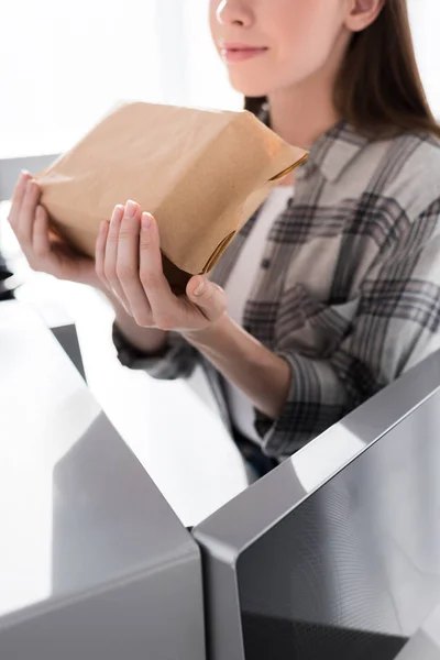 Vue recadrée de la femme tenant sac en papier avec pop-corn près du micro-ondes dans la cuisine — Photo de stock