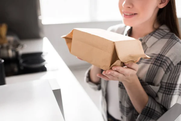 Vue recadrée d'une femme souriante tenant un sac en papier avec du maïs soufflé près du micro-ondes dans la cuisine — Photo de stock