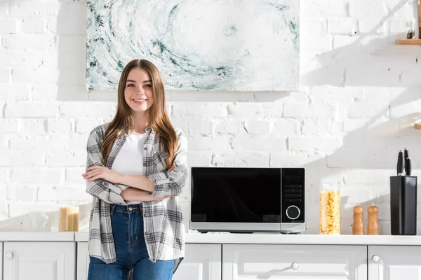 Mujer sonriente y atractiva de pie cerca de microondas en la cocina - foto de stock