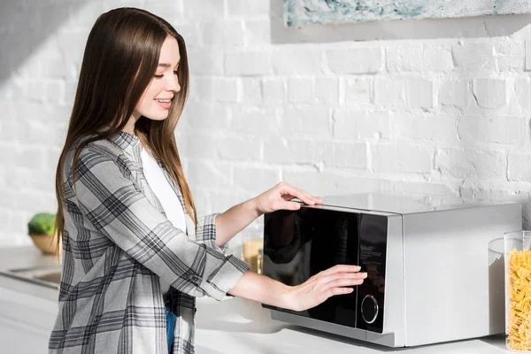 Femme souriante et attrayante en chemise utilisant micro-ondes dans la cuisine — Photo de stock