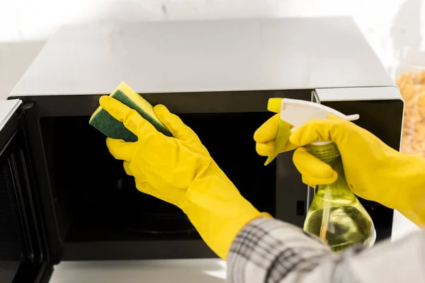 Vista recortada de la mujer en guantes de goma limpieza microondas con esponja - foto de stock