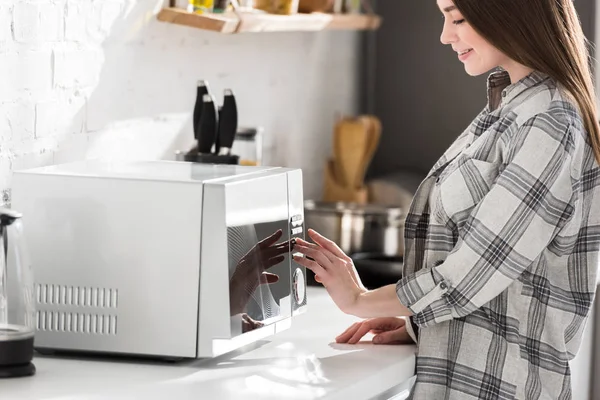 Обрезанный вид улыбающейся женщины в рубашке с помощью микроволновки на кухне — стоковое фото