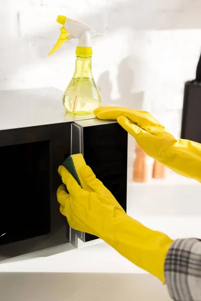 Cropped view of woman in rubber gloves cleaning microwave with sponge — Stock Photo