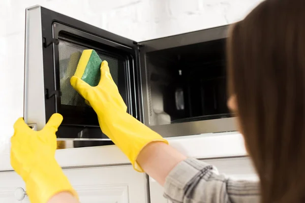 Vista recortada de la mujer en guantes de goma limpieza microondas con esponja - foto de stock