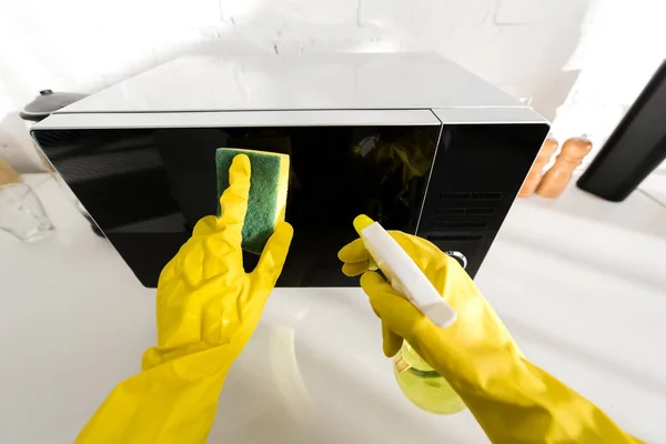 Cropped view of woman in rubber gloves cleaning microwave with sponge — Stock Photo