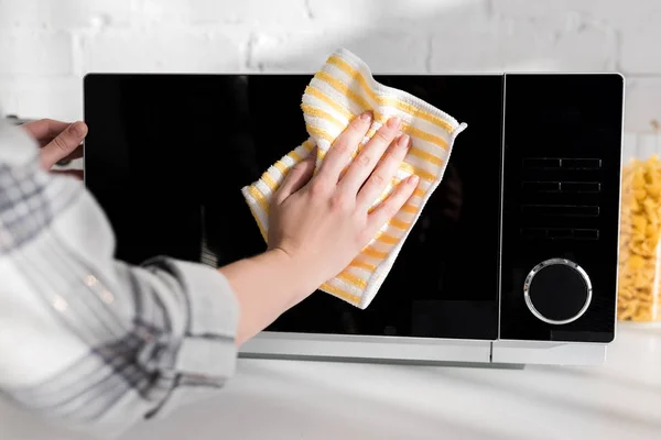 Vista cortada de mulher limpeza de microondas com pano na cozinha — Fotografia de Stock