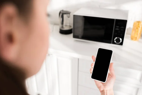 Vista recortada de la mujer usando teléfono inteligente cerca de microondas en la cocina — Stock Photo