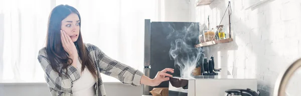 Plano panorámico de mujer asustada y atractiva mirando microondas roto en la cocina - foto de stock