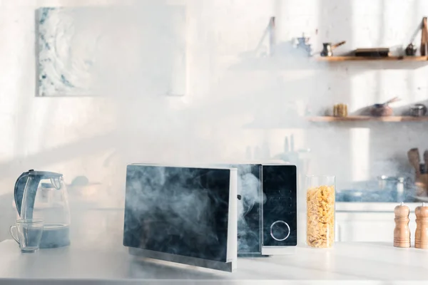 Electric kettle, pasta, broken and steamy microwave on table in kitchen — Stock Photo