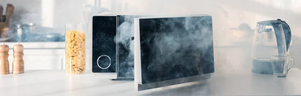 Panoramic shot of broken and steamy microwave on table in kitchen — Stock Photo