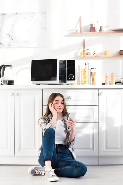 Mujer triste usando teléfono inteligente cerca de microondas roto en la cocina - foto de stock