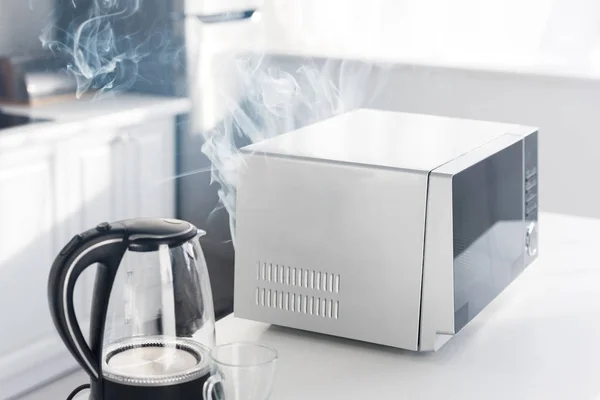Электрический чайник, сломанная и паровая микроволновая печь на столе на кухне — стоковое фото