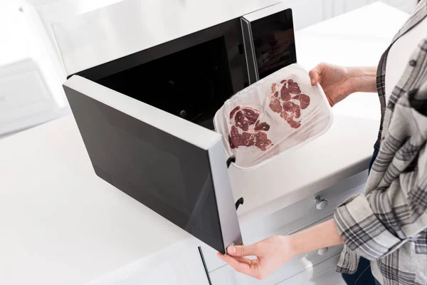 Cropped view of woman putting meat into microwave in kitchen — Stock Photo