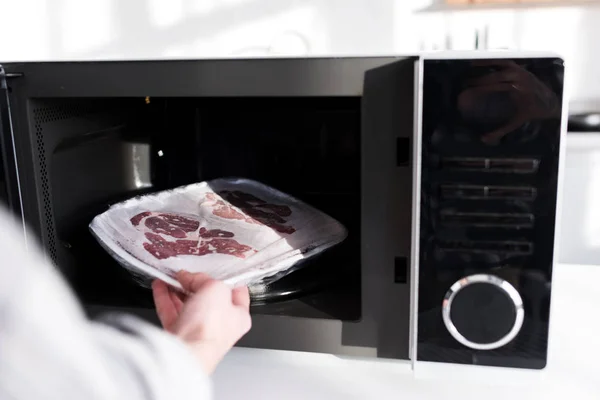 Cropped view of woman putting meat into microwave in kitchen — Stock Photo