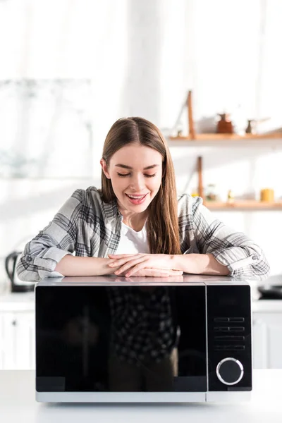 Smiling and attractive woman looking at microwave in kitchen — Stock Photo