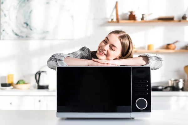 Smiling and attractive woman lying on microwave in kitchen — Stock Photo