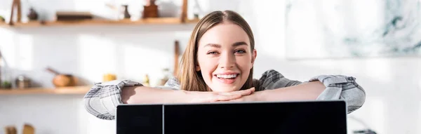 Plano panorámico de mujer sonriente y atractiva de pie cerca de microondas en la cocina - foto de stock