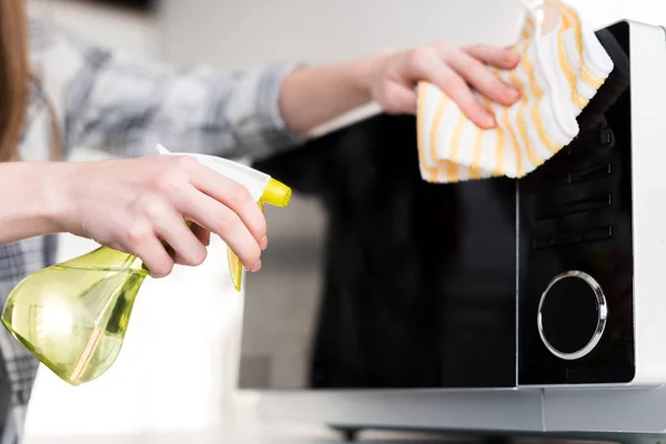 Ausgeschnittene Ansicht einer Frau, die in der Küche Mikrowelle mit Lappen reinigt — Stockfoto